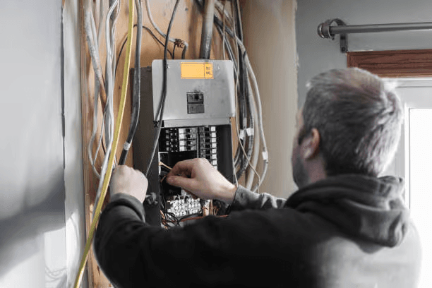 Electrician performing wiring and connection work inside an open residential electrical panel during home renovation
