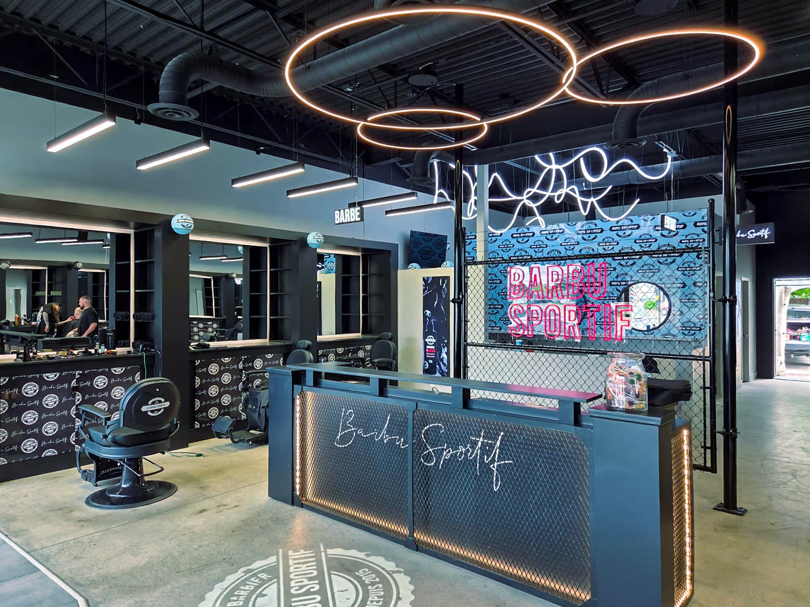 Modern barbershop interior with barber stations, chairs, reception counter, circular pendant lighting and industrial decor
