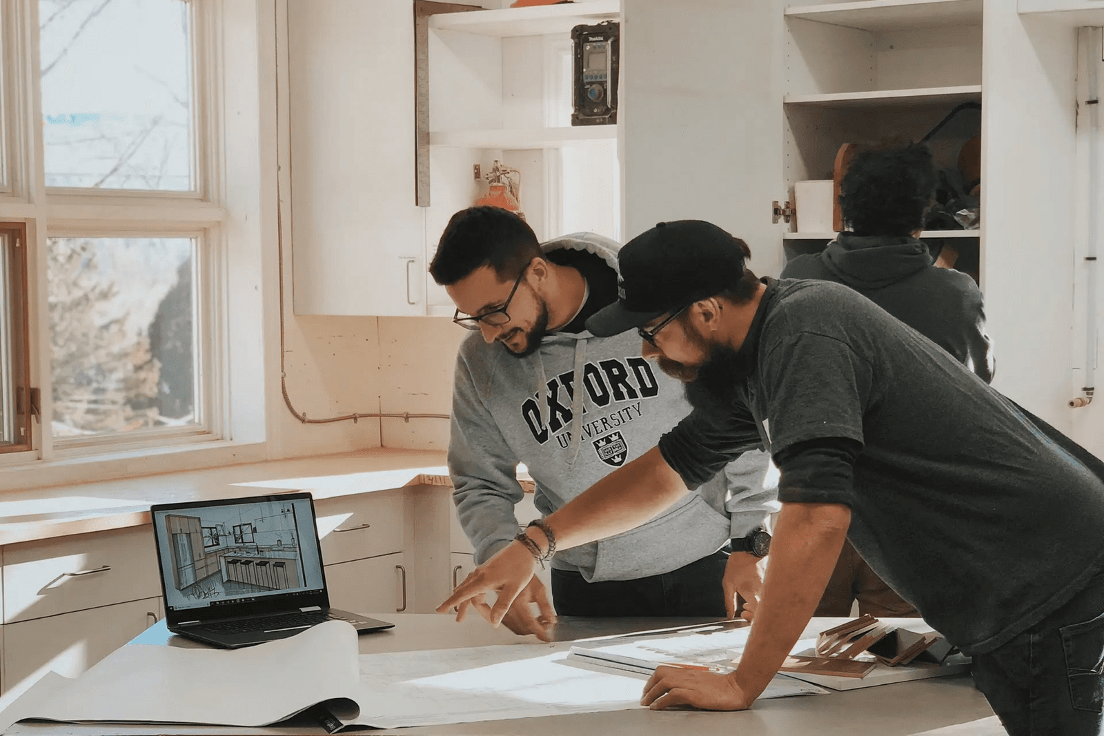 Renovation professionals reviewing plans and a kitchen design on a laptop inside a residential space under remodeling.