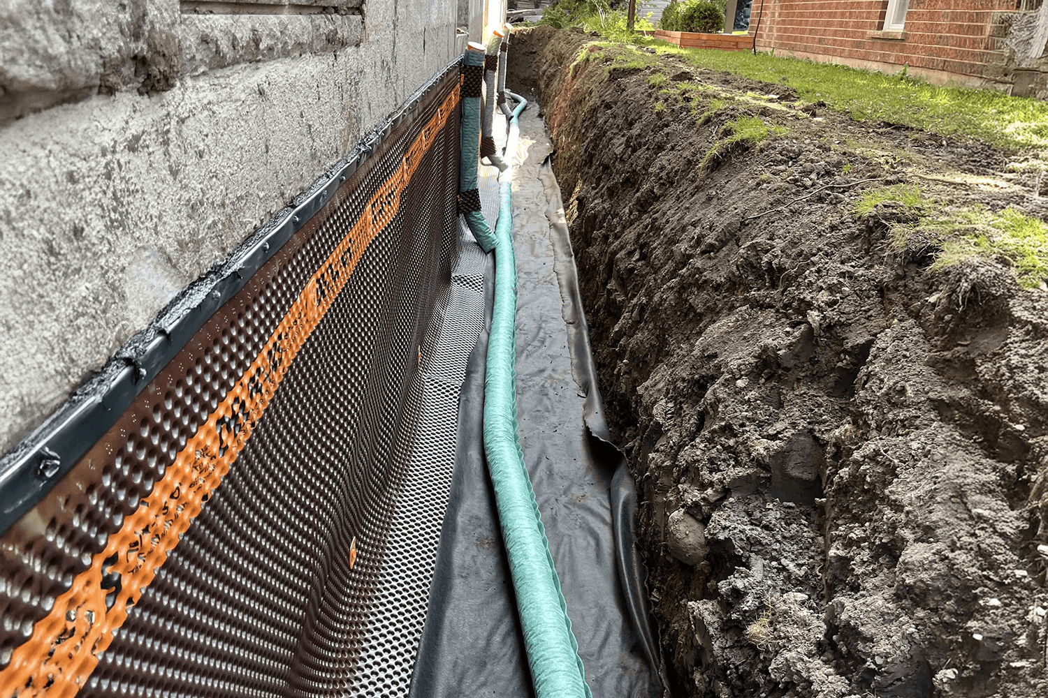 Foundation drain installation with a waterproofing fabric against a house's foundation