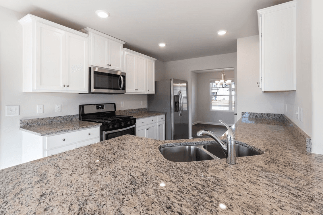 Bright residential kitchen with white cabinets, large granite countertops, double sink, stainless steel appliances, and recessed lighting.