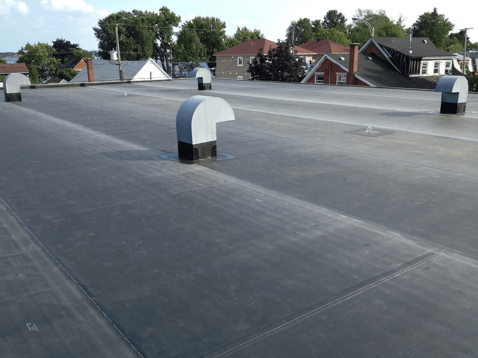 Flat roof covered with a gray waterproofing membrane and several ventilation outlets on a residential building in an urban area