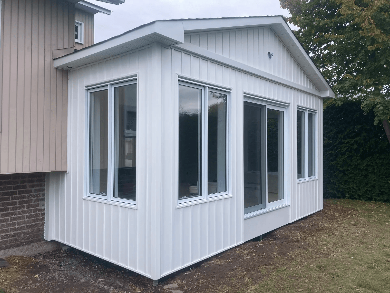 Modern residential home extension with white exterior siding, large windows and glass door overlooking the backyard