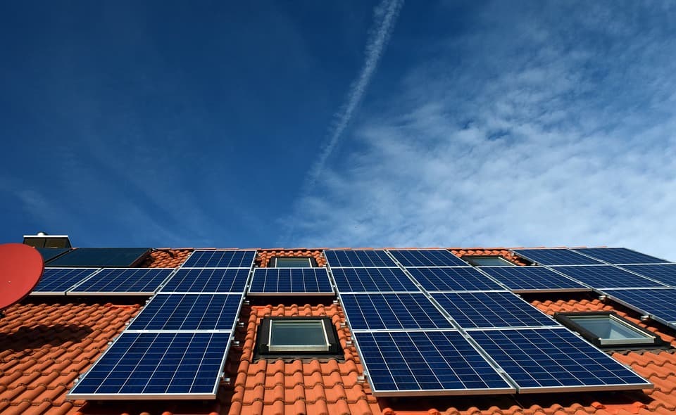 Low-angle view of photovoltaic solar panels installed on the red tile roof of a residential home under a blue sky
