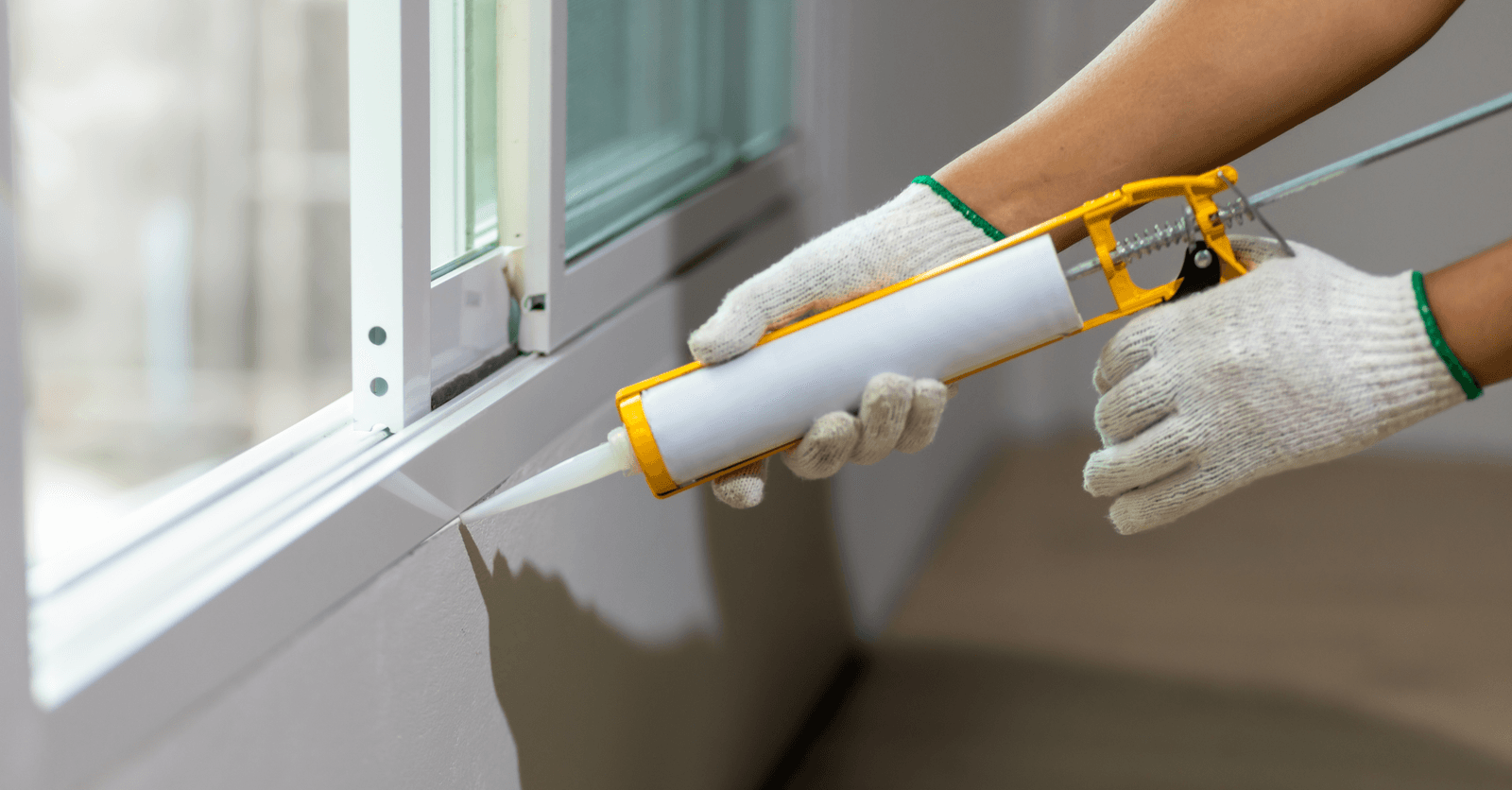 Person applying caulking around a window to improve thermal insulation