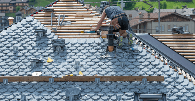A man installing slate slabs on a pitched roof, making the slate roof covering.